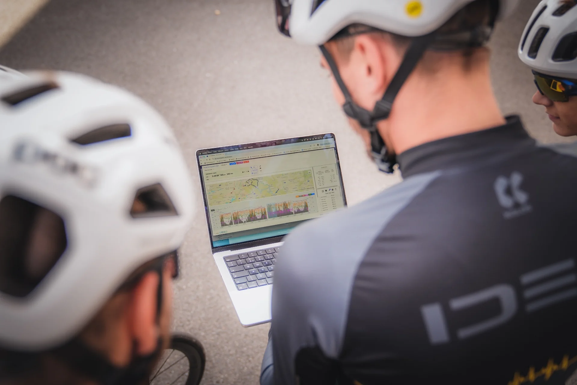 Členové týmu v cyklistických helmách společně procházejí záznam tréninku na notebooku